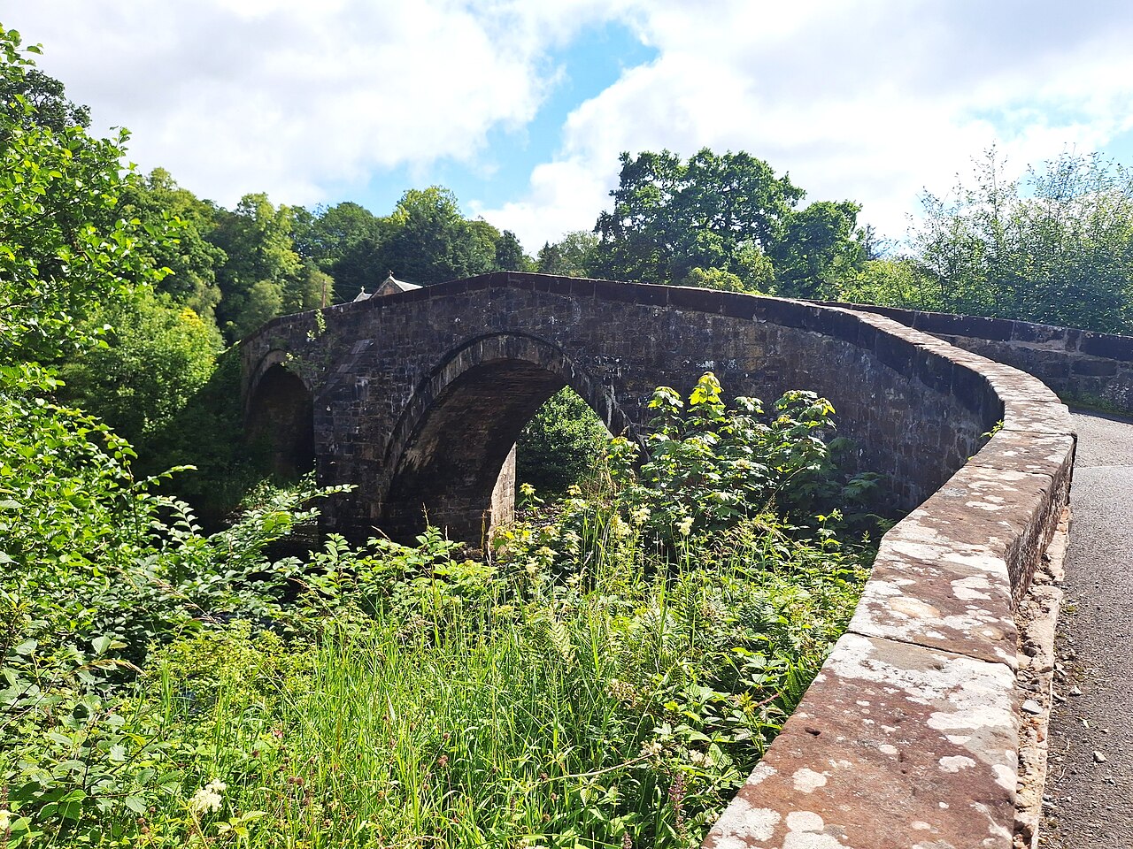 The stone arches and curved parapet of Sorn Old Bridge, surrounded by summer greenery